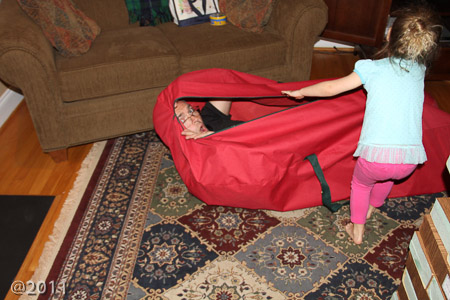 Penny unzipping Andrew from the Giant Jenga bag
